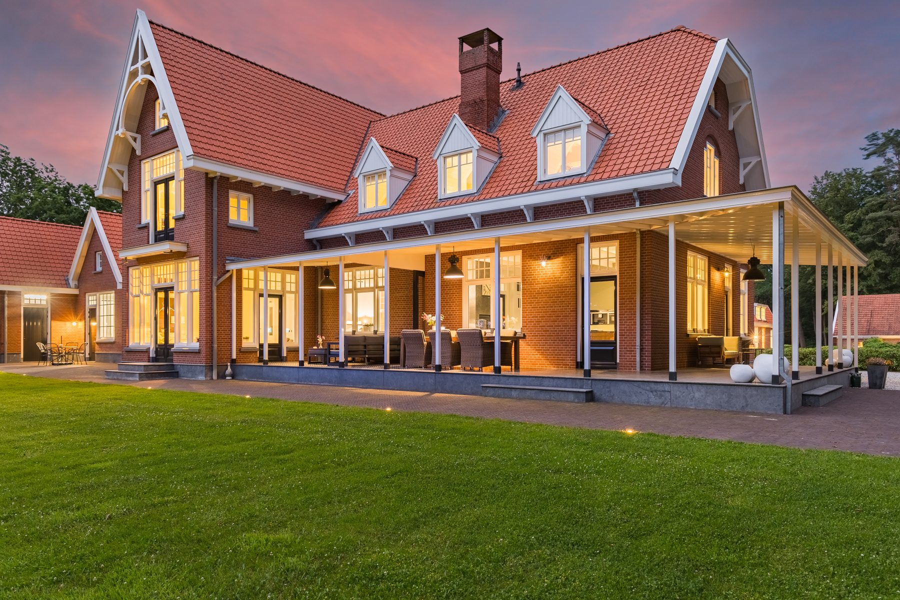 Het landhuis bij avond, met de verlichte veranda langs de gevel