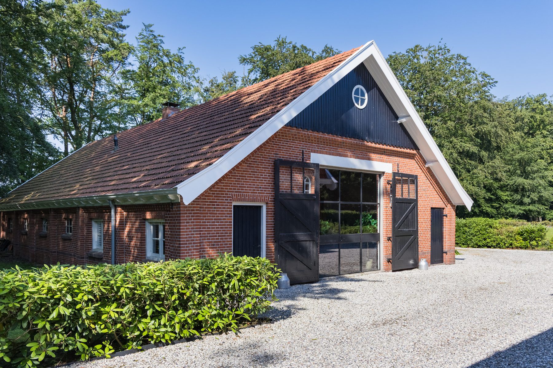 De woonboerderij: zwarte houten topgevel met rond oculusraam boven de brede staldeuren