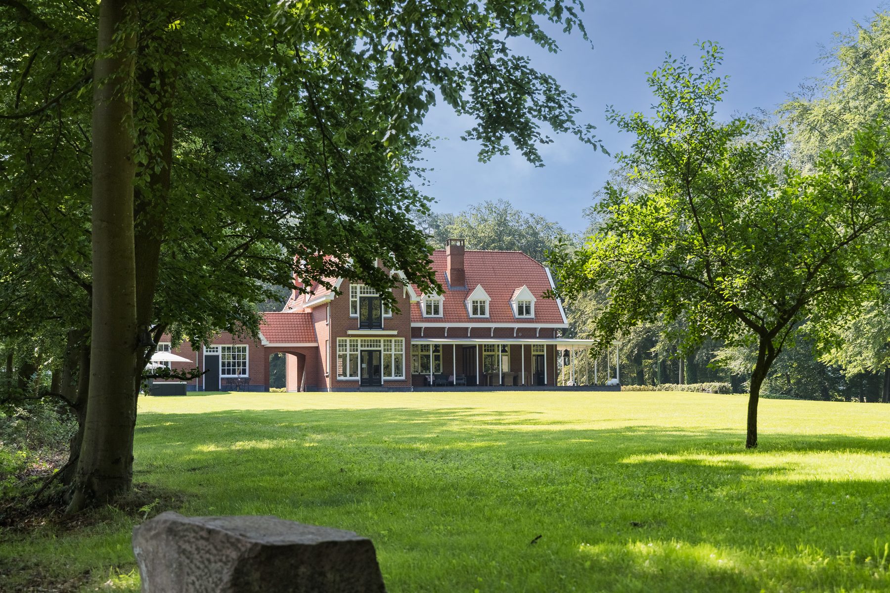 Het landhuis gezien vanaf de rand van het gazon, onder de bomen door