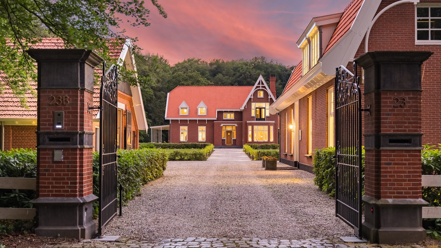 De toegangspoort van het landgoed in avondlicht, met de oprijlaan en het landhuis erachter
