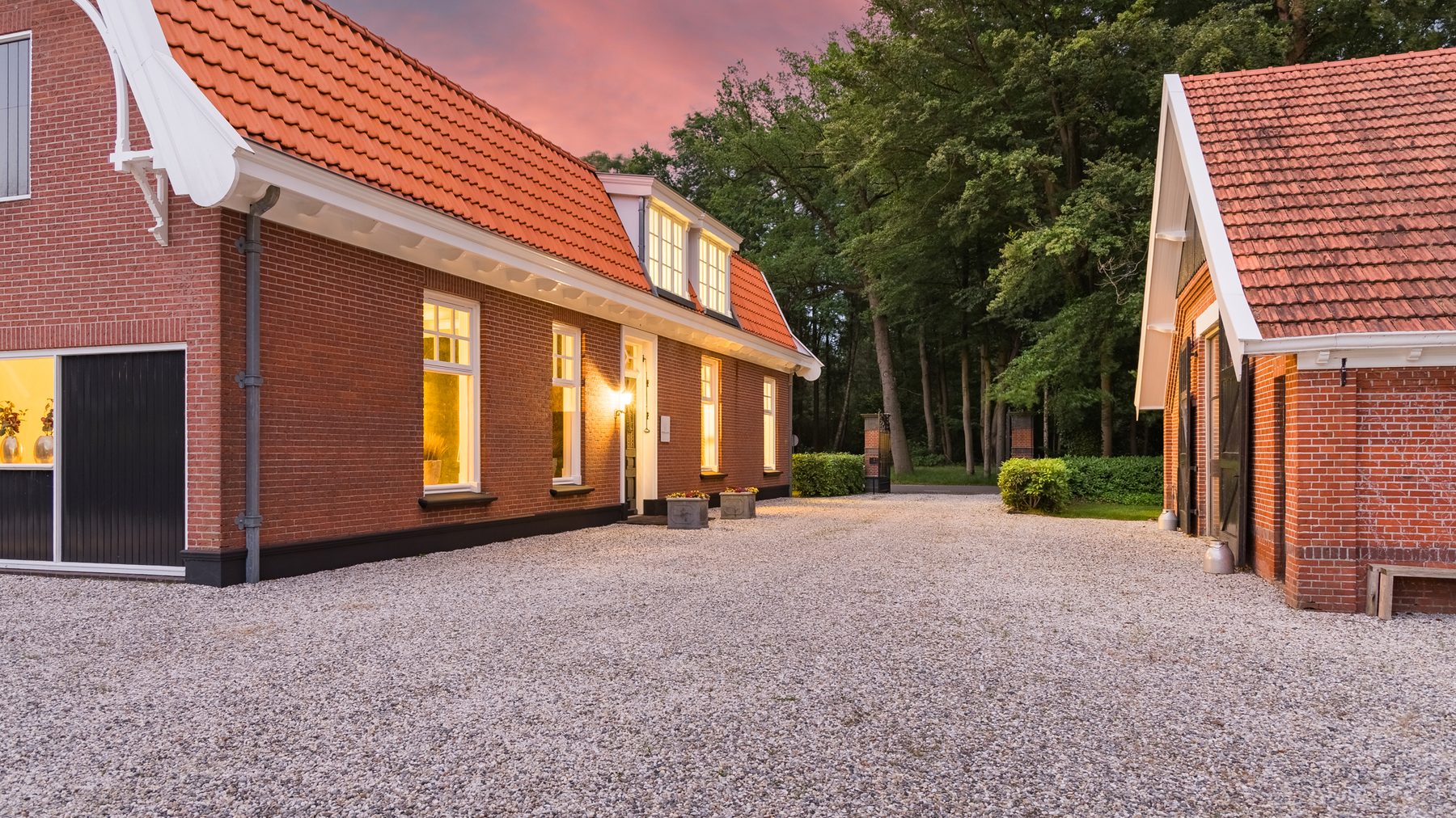 De lange gevel van De Loods bij avond, met verlichte vensters langs het grind
