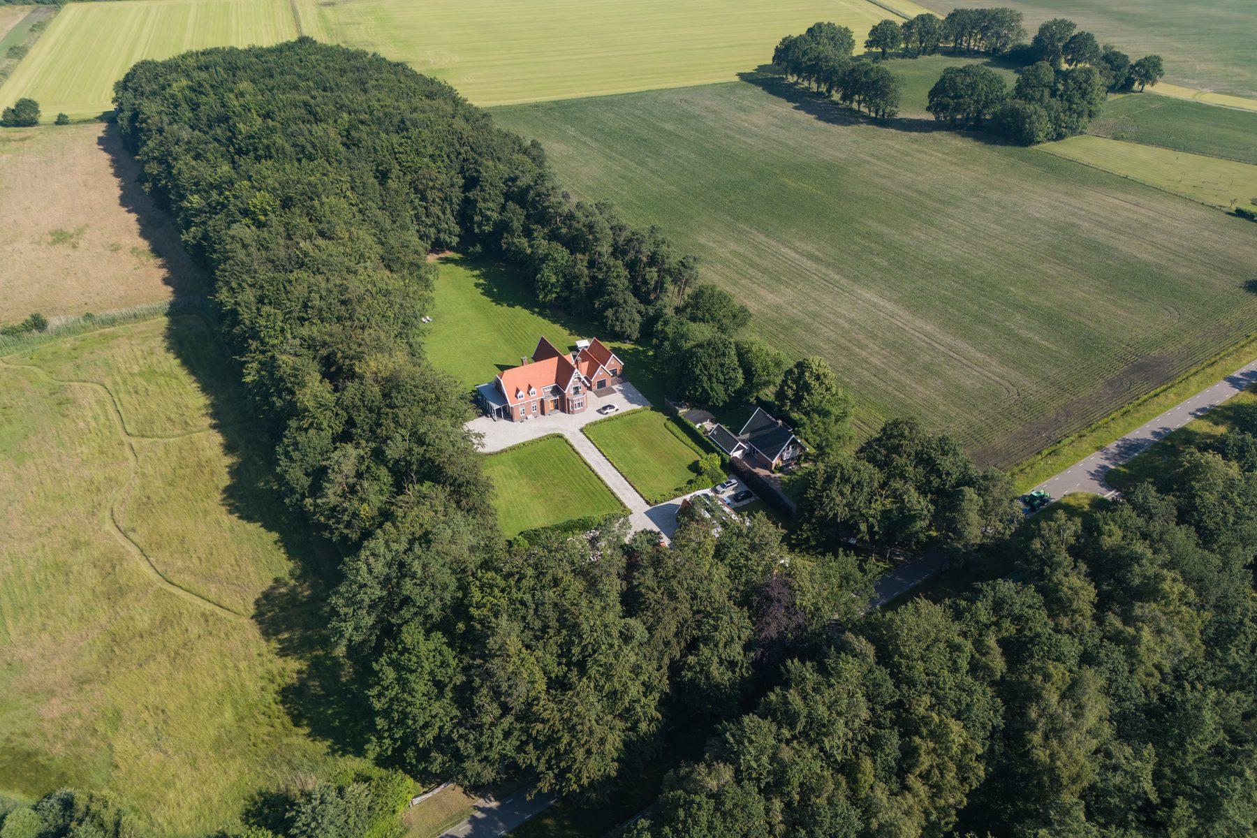 Luchtfoto van het landgoed: het landhuis en de bijgebouwen, omzoomd door het beukenbos