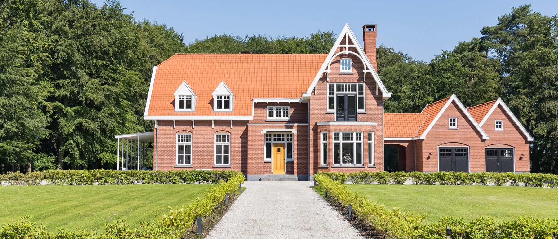 Het landhuis frontaal gezien over het gazon, met de gesnoeide hagen naar de voordeur