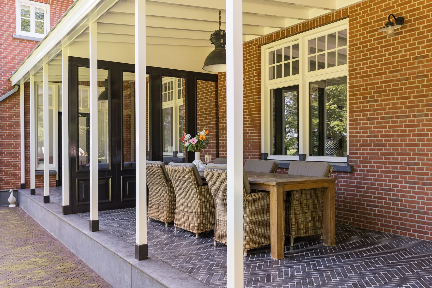 De veranda langs de gevel, met eettafel onder de houten overkapping